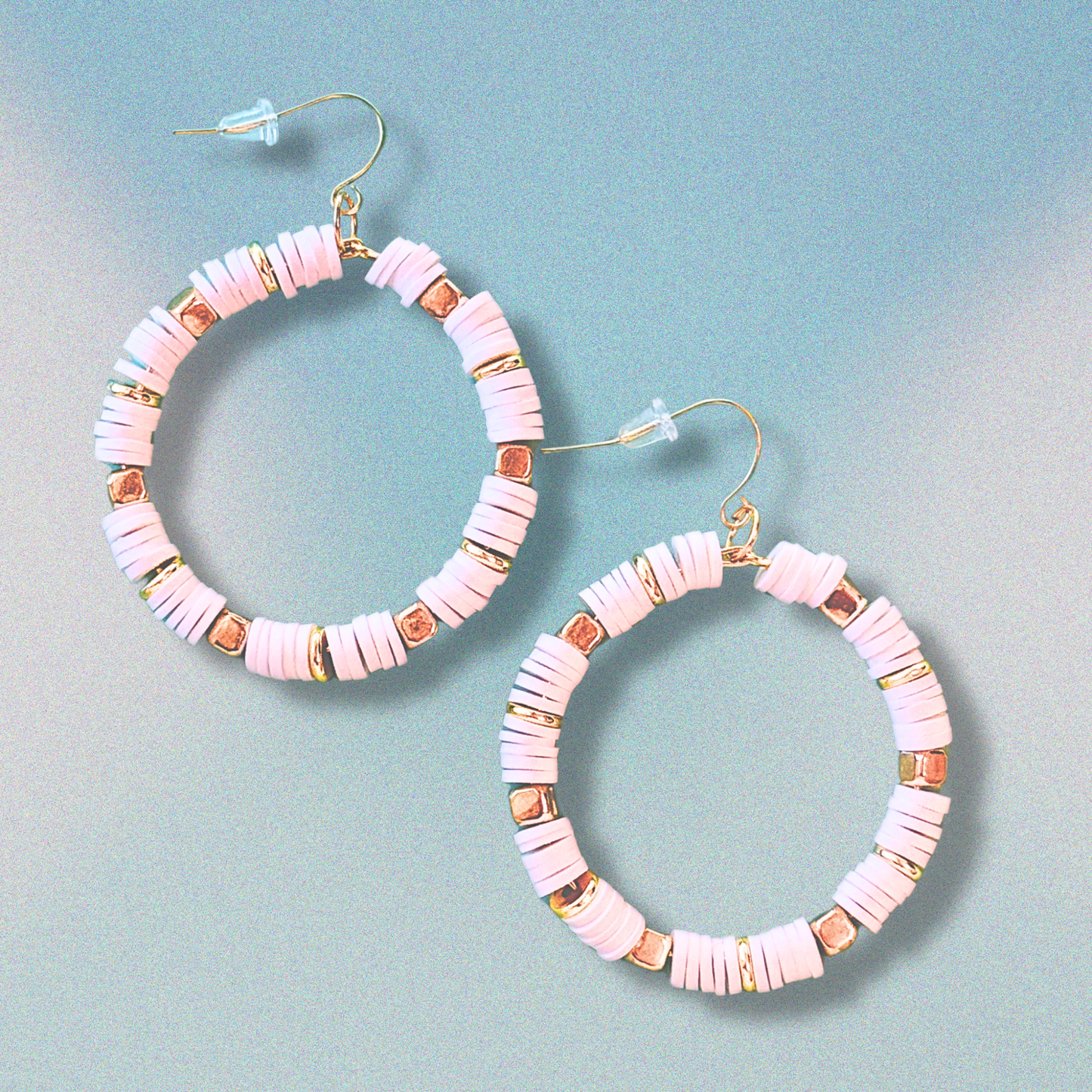 A pair of white and gold hoop earrings with heishi beads, inspired by coastal elegance, displayed against a soft blue gradient background for a minimal yet luxurious look.