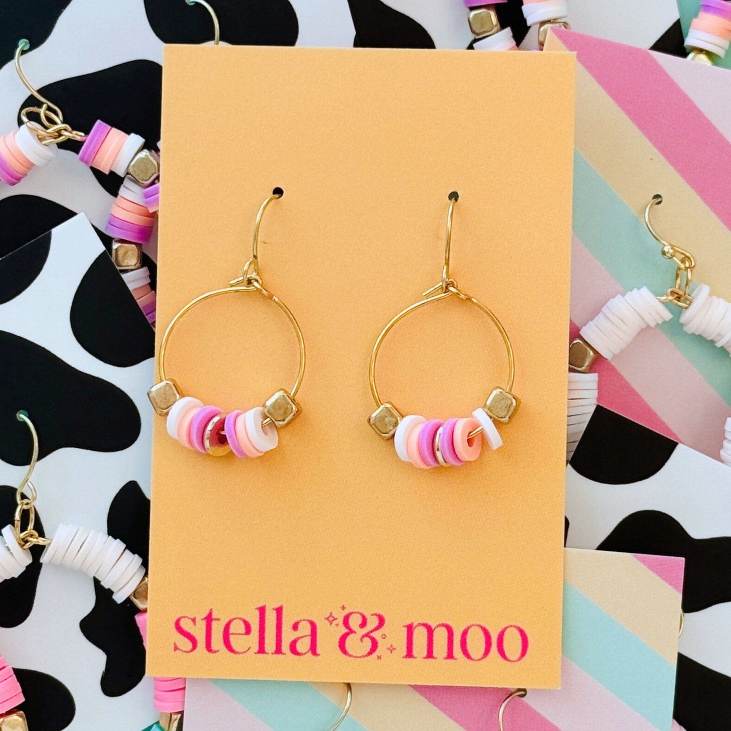 A pair of delicate gold mini hoop earrings featuring soft pink and white beaded accents, presented on a warm-toned Stella & Moo branded card, perfect for a fun yet minimal statement look.