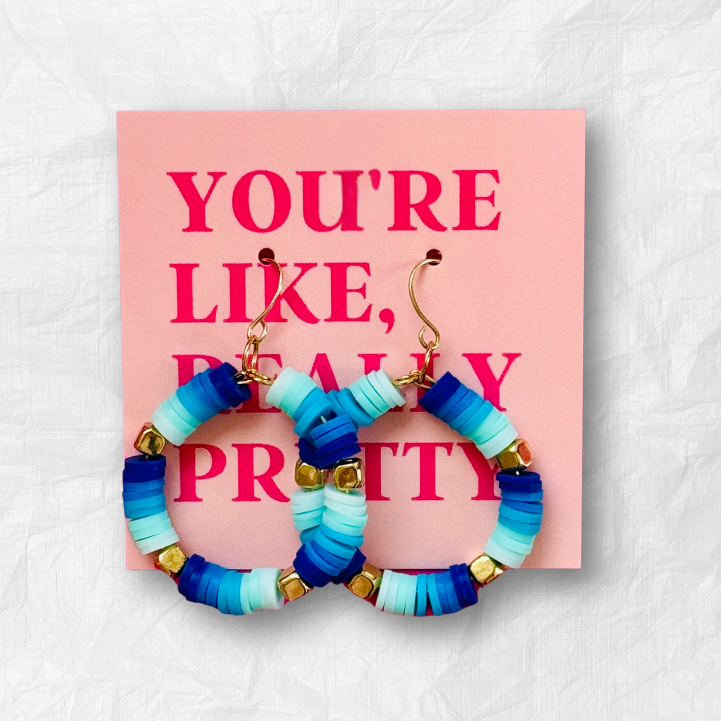 A pair of handcrafted blue and gold beaded hoop earrings with ocean-inspired hues, displayed on a neutral background for a bold yet elegant look.