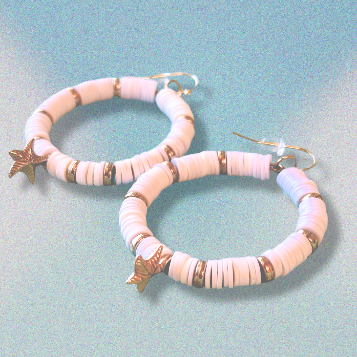 A pair of white and gold starfish hoop earrings with coastal-inspired heishi beads and shimmering accents, designed for a beachy and elegant aesthetic against a soft blue background.