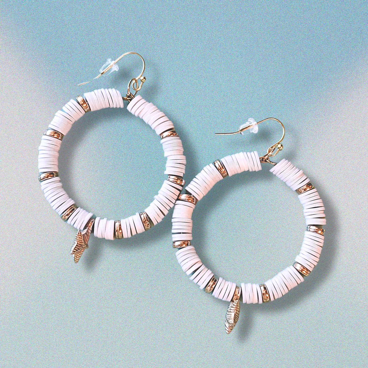 A pair of white and gold starfish hoop earrings with coastal-inspired heishi beads and shimmering accents, designed for a beachy and elegant aesthetic against a soft blue background.