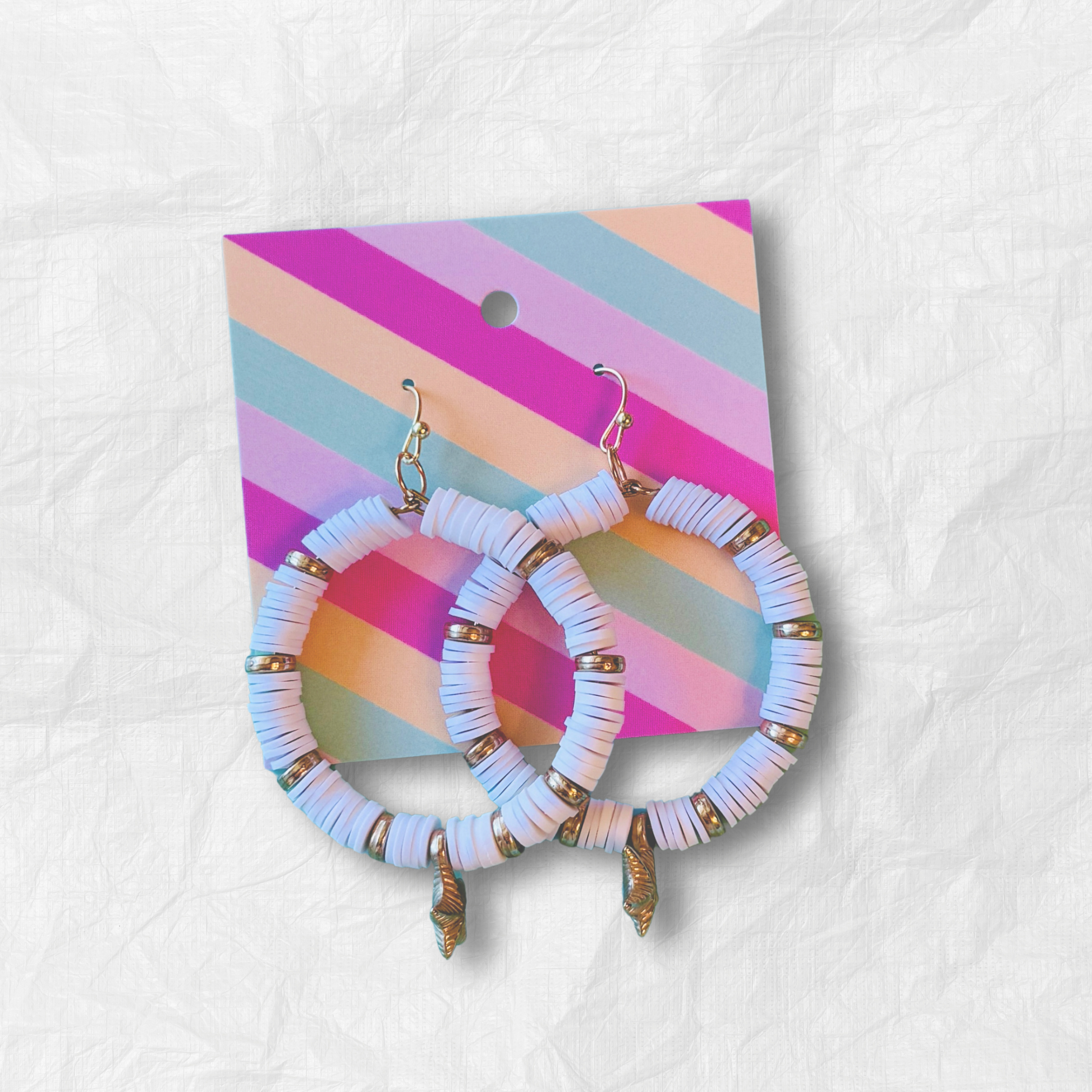 A pair of white and gold starfish hoop earrings with coastal-inspired heishi beads and shimmering accents, designed for a beachy and elegant aesthetic against a soft blue background.