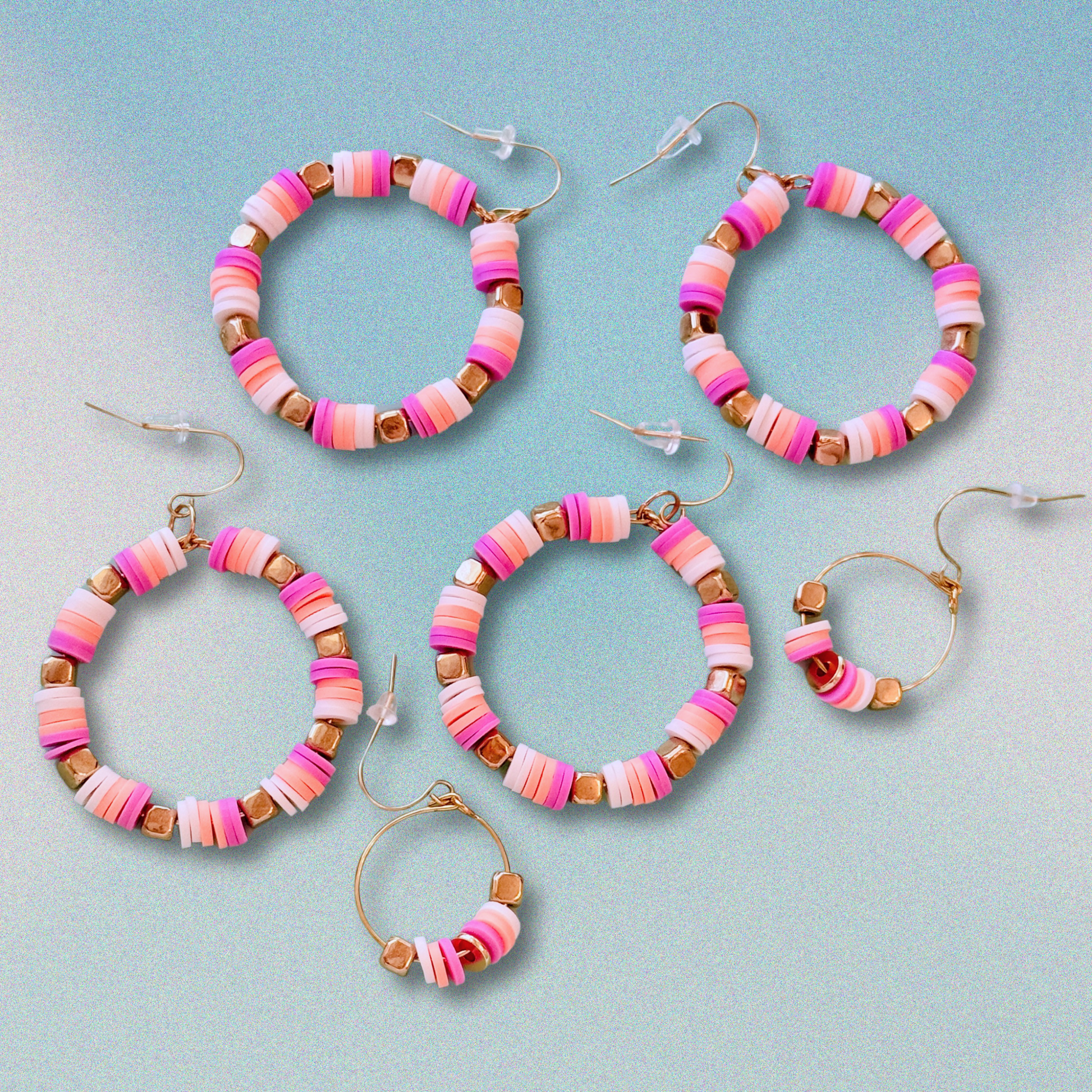 A close-up of handcrafted hoop earrings featuring soft pruple, creamsickle orange, and white beads with gold accents, inspired by the colors of French macarons, displayed on a soft blue background for a fun and playful statement look.