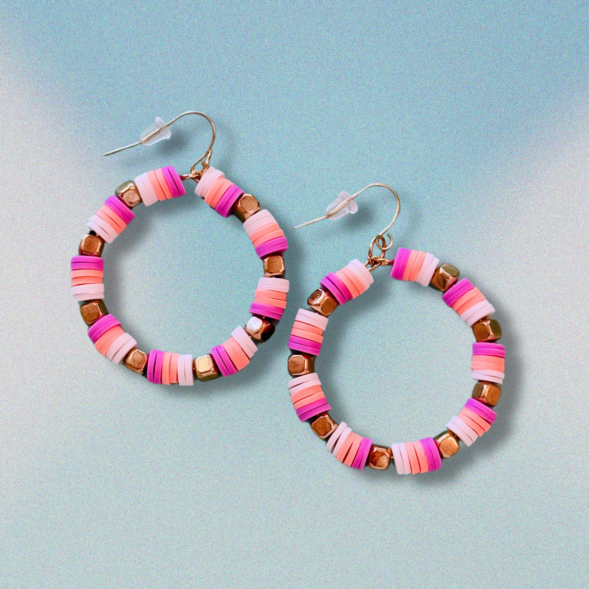 A close-up of handcrafted hoop earrings featuring soft pruple, creamsickle orange, and white beads with gold accents, inspired by the colors of French macarons, displayed on a soft blue background for a fun and playful statement look.