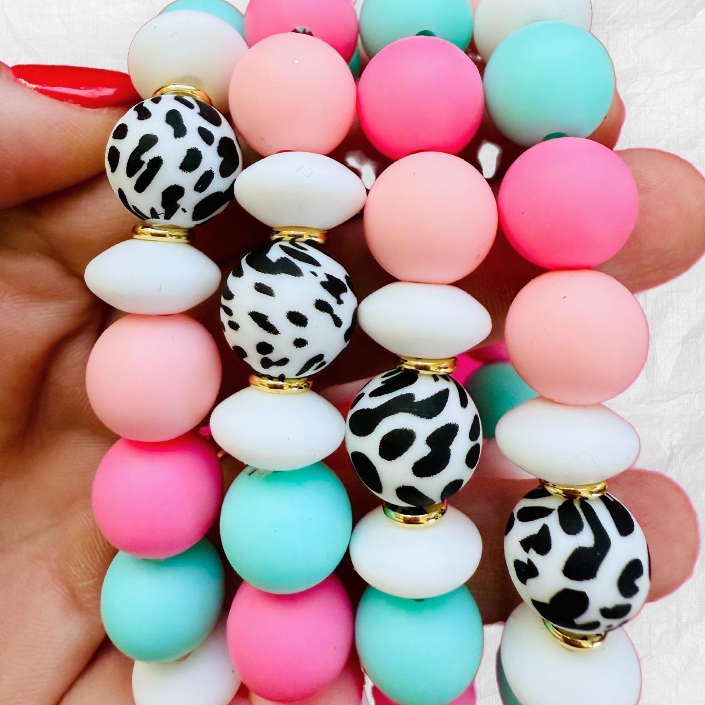Hand holding vibrant silicone bead bracelets in pastel pink, aqua, and white with black-and-white animal print beads, creating a playful and stylish accessory look.