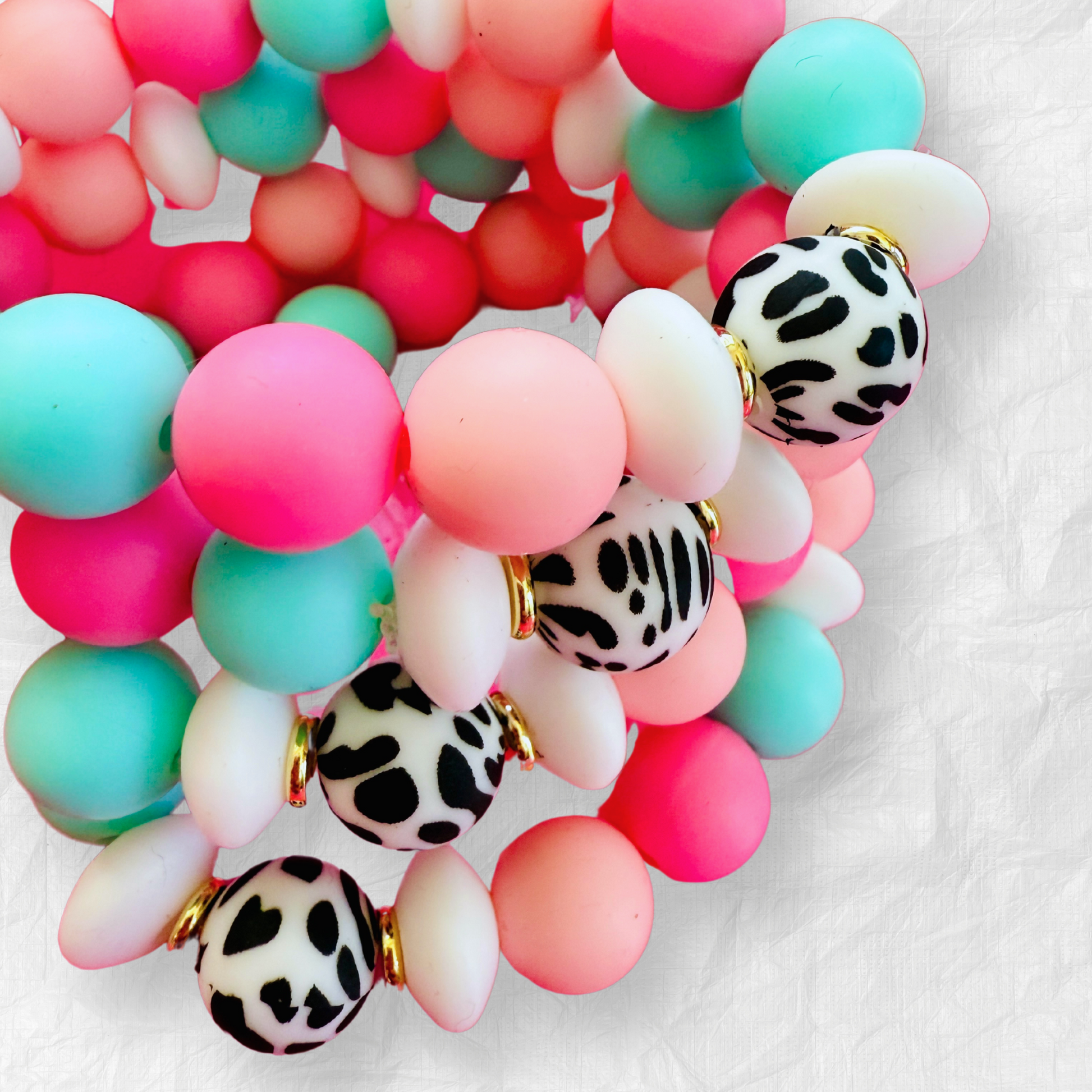 Hand holding vibrant silicone bead bracelets in pastel pink, aqua, and white with black-and-white animal print beads, creating a playful and stylish accessory look.