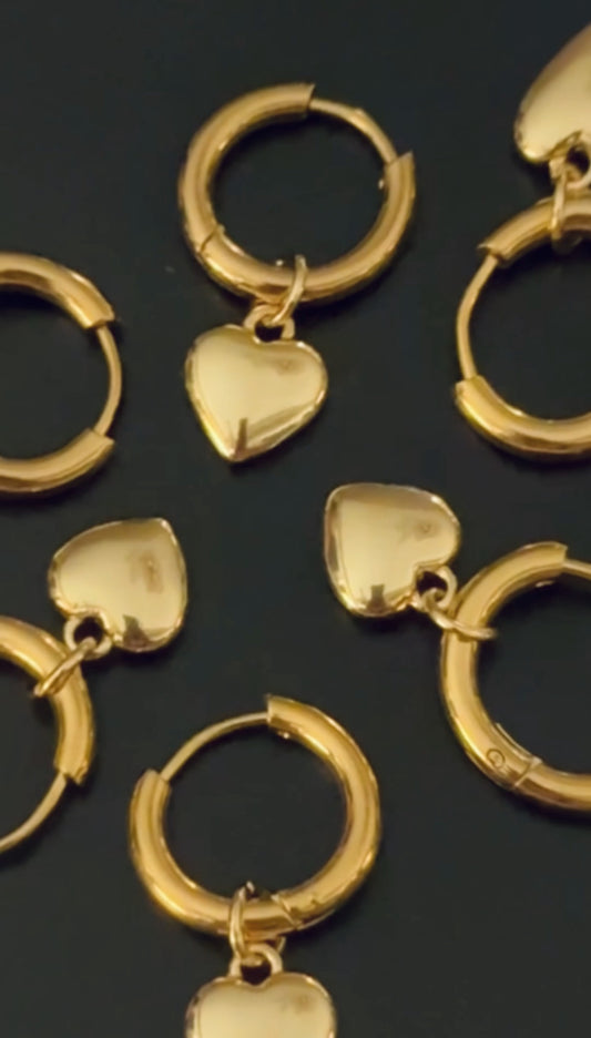 Gold hoop earrings with heart pendants on a dark background